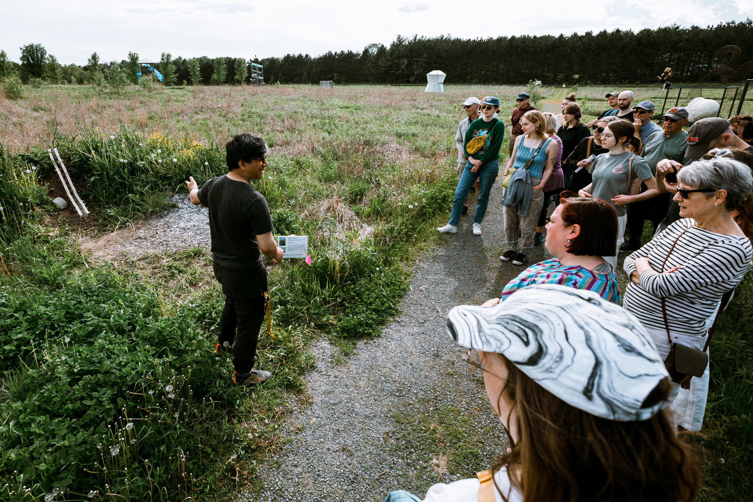 A person speaks to a crowd and points to a land feature outdoors.