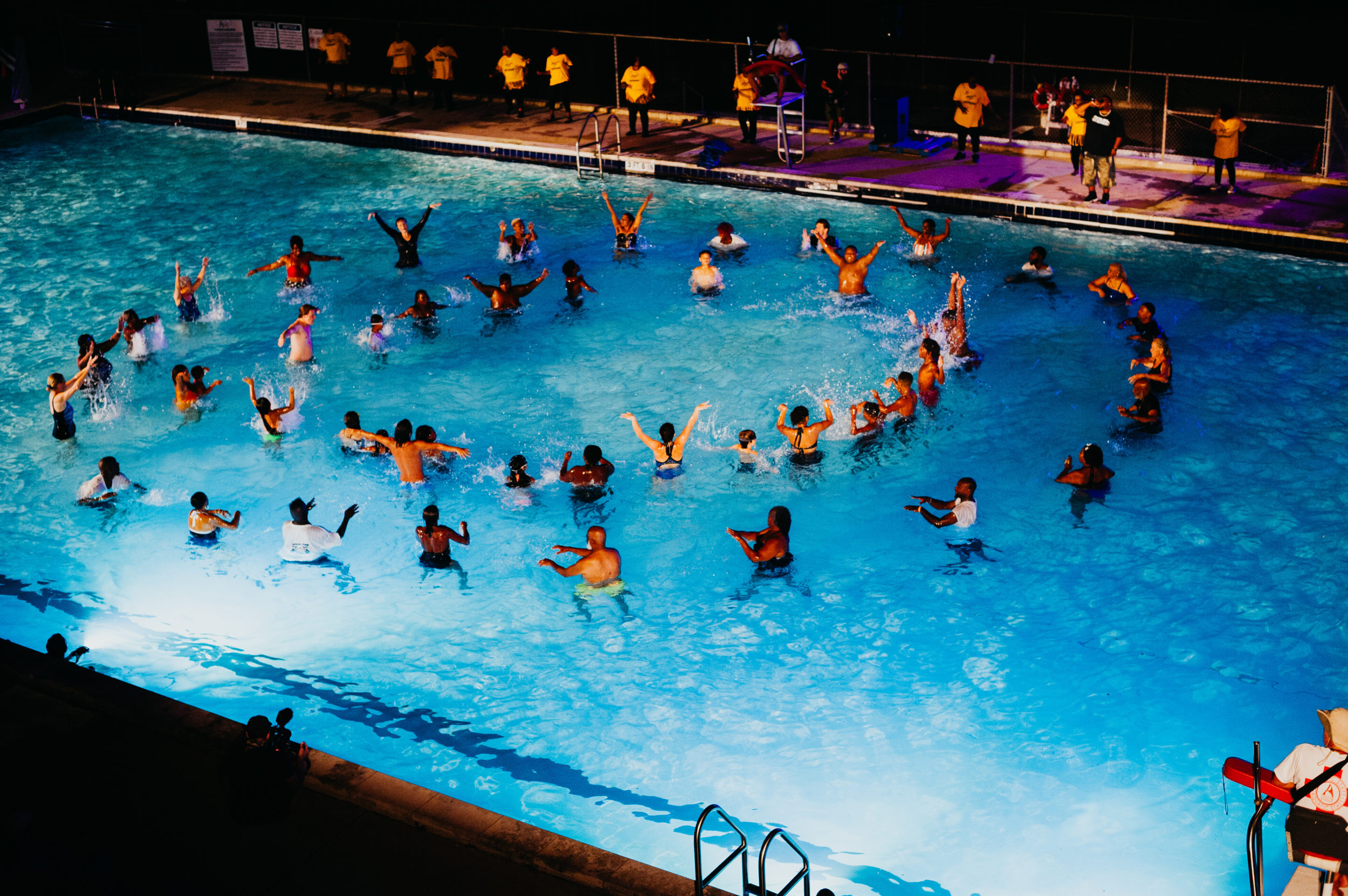 Swimmers stand in circles in a pool at night