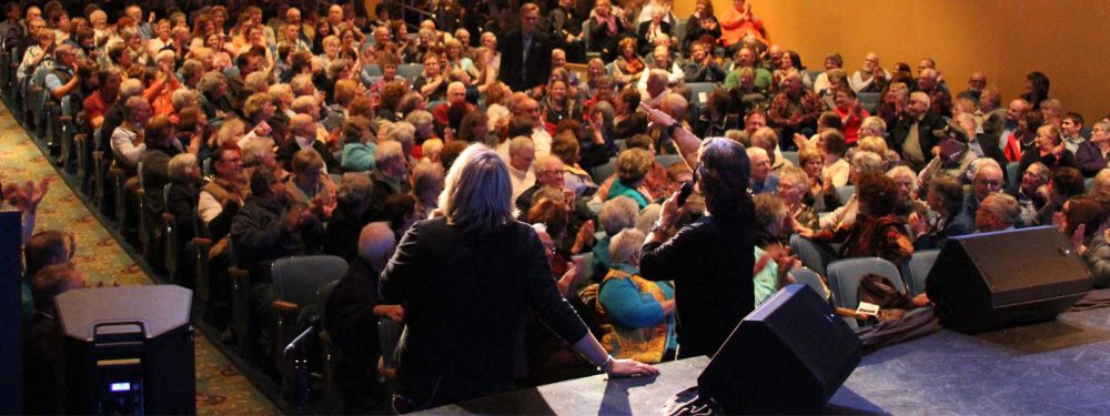A crowd of people in a theater watch performers