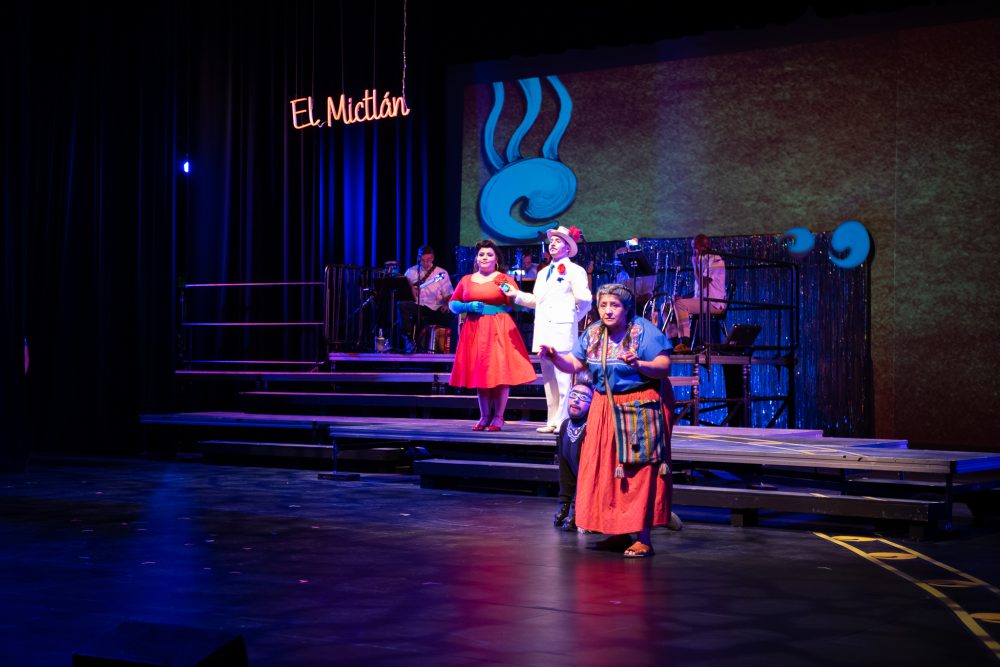 Four actors on stage wearing bright red and white clothes performing Departera: the road to the afterlife.