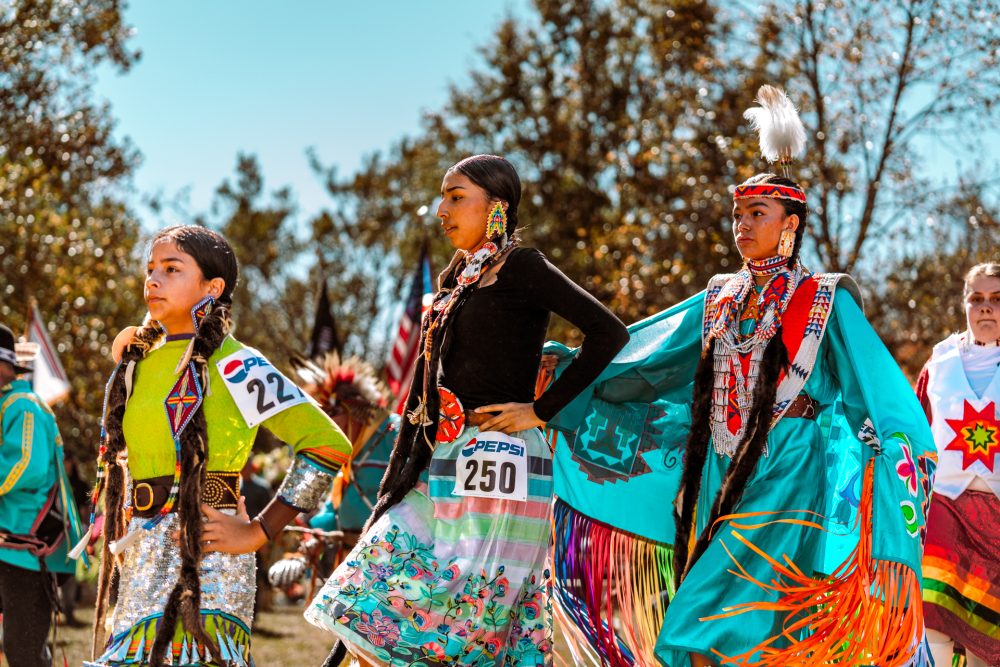 Three native american dancers perform in regalia at an outdoors pow wow